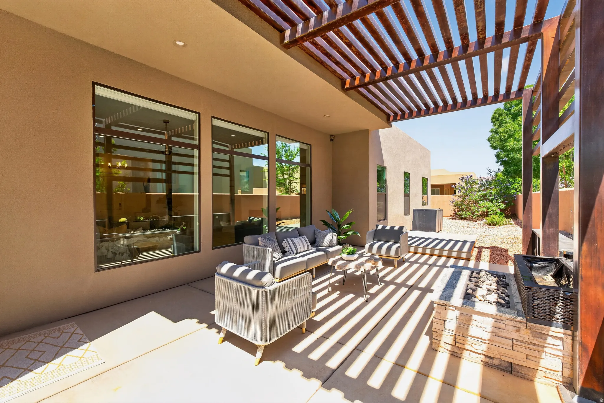 Expansive patio featuring a wooden pergola, stone-clad fire pit, large format tile flooring, and outdoor lighting for evening get togethers.