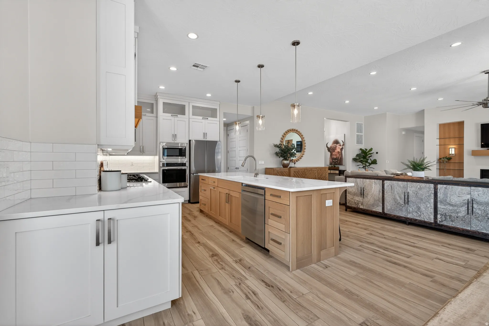 Open-concept kitchen featuring an expansive island, white shaker cabinetry, stainless steel appliances, and wood-finish flooring