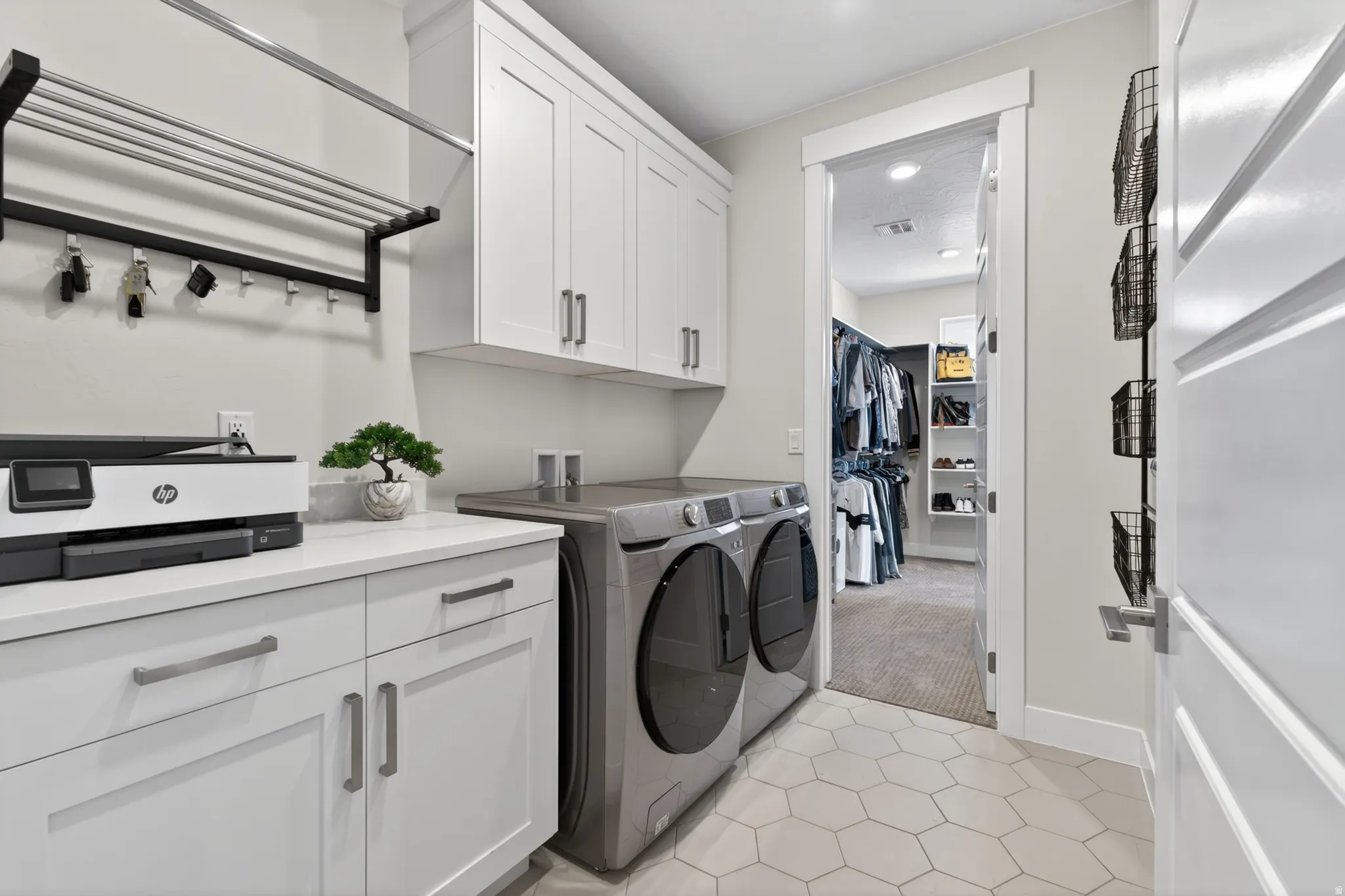 Dedicated laundry area attached to master suite, featuring hexagon tile flooring, white shaker cabinetry with brushed nickel hardware, and light-tone countertops