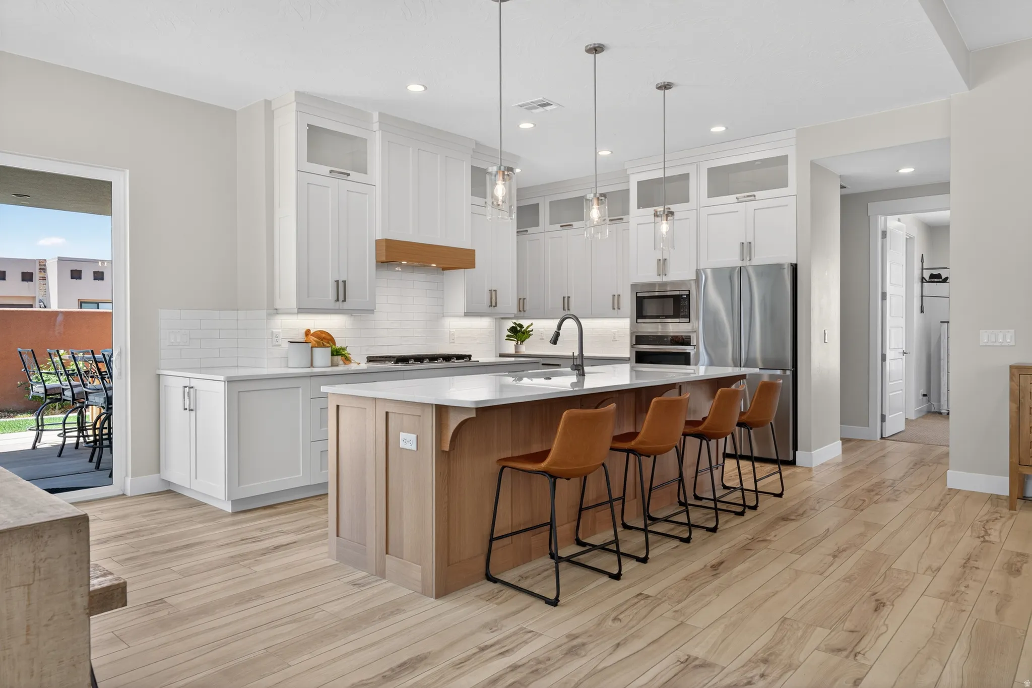 Modern kitchen featuring light wood-finish flooring, white perimeter cabinetry with glass-front upper cabinets, a white subway tile backsplash, and stainless steel appliances