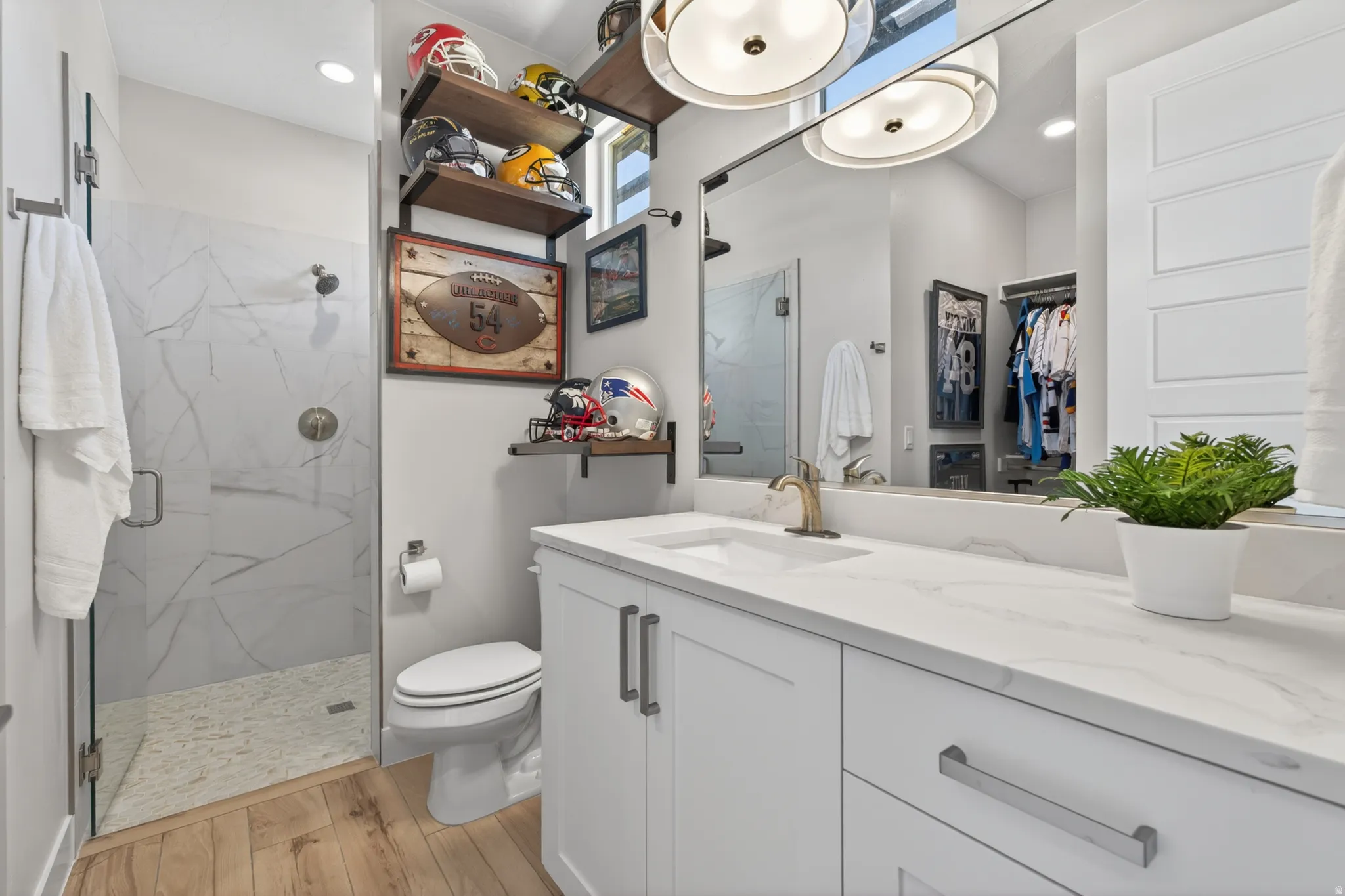 Bathroom featuring a glass-enclosed shower with large format marble-look tile, a single vanity with a white countertop, light wood-finish flooring, and built-in shelving
