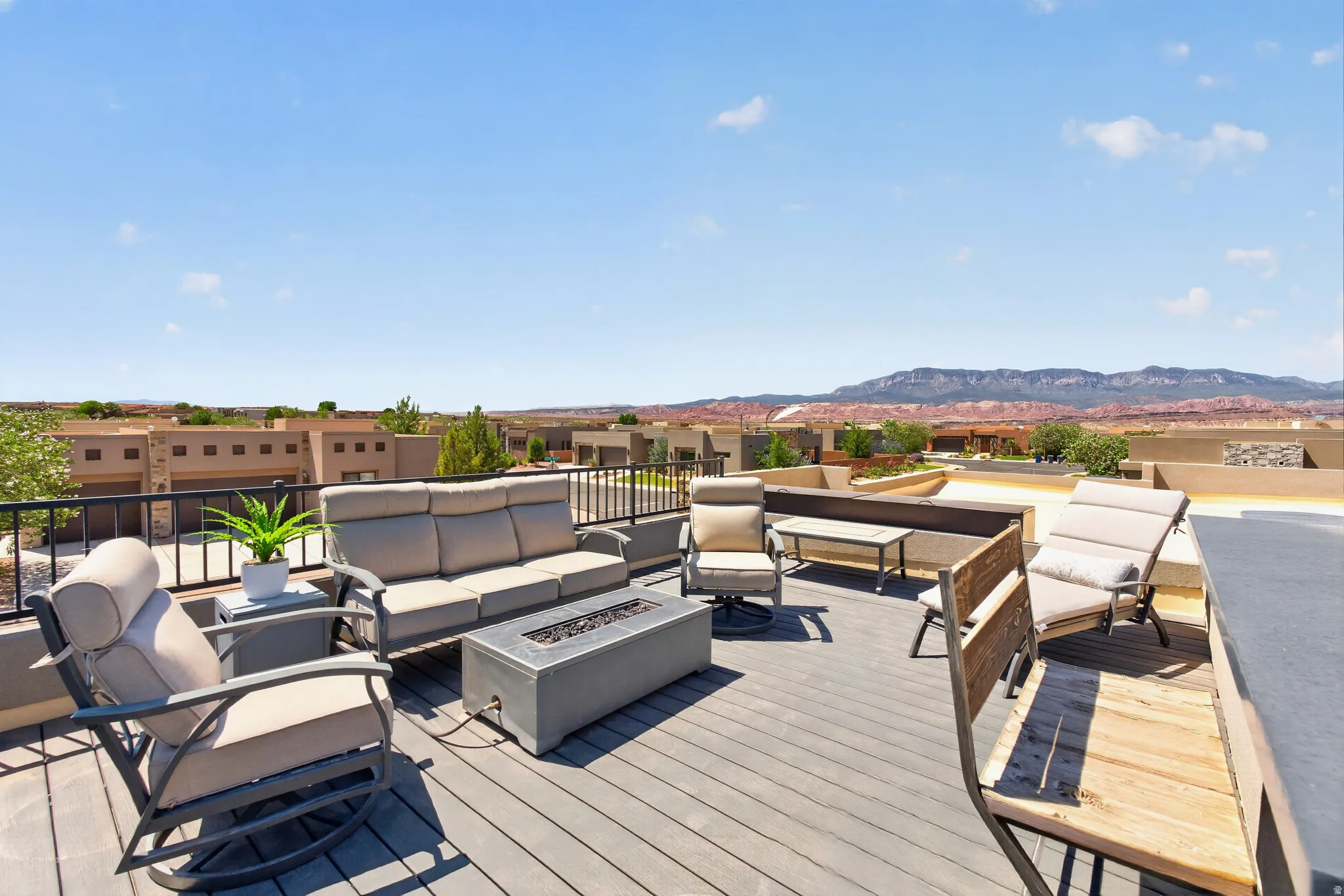 Expansive rooftop deck featuring composite decking, a built-in privacy wall, black metal railings, a stone-finish fire pit, built in bar and distant mountain scenery. Perfect for evening gatherings and star gazing.