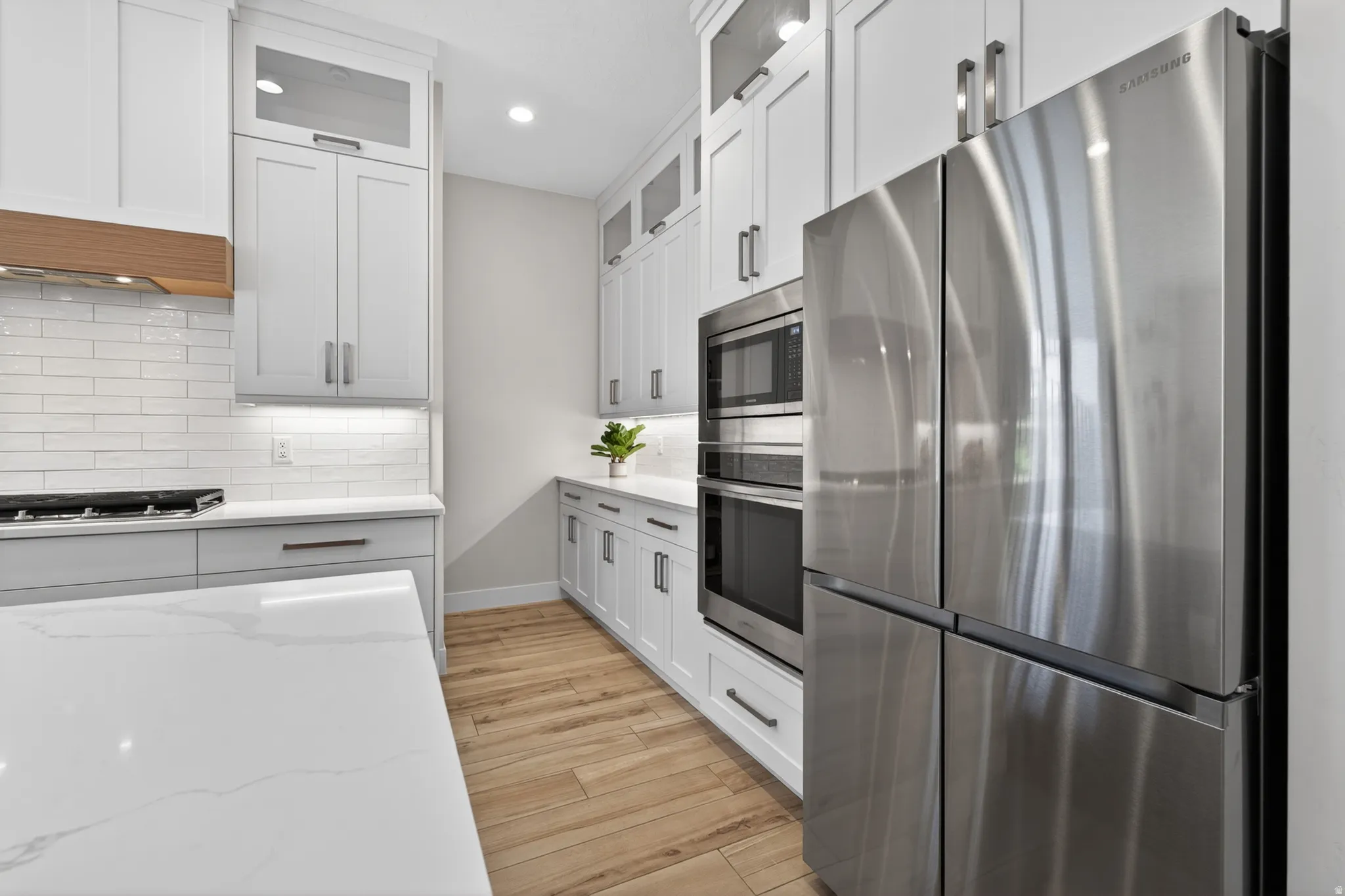 Kitchen featuring white shaker cabinetry with transom windows at top, a built-in stainless steel double oven, a stainless-steel refrigerator, and white subway tile backsplash