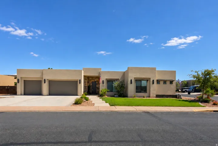 Contemporary stucco exterior featuring a stone accent entry, two-car garage, concrete driveway, and front landscaping with grass and desert plants