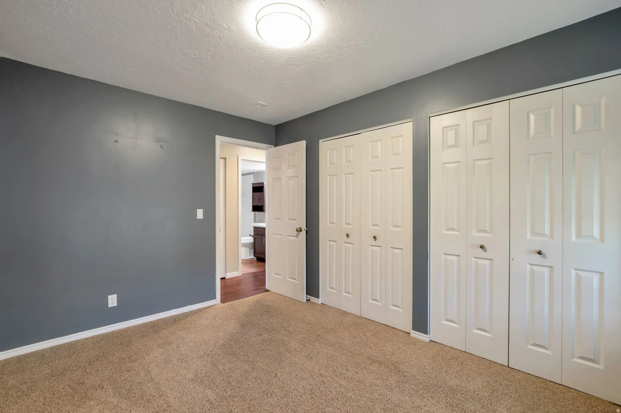 Carpeted room with a ceiling-mounted light fixture, two sets of bi-fold closet doors, and painted gray walls