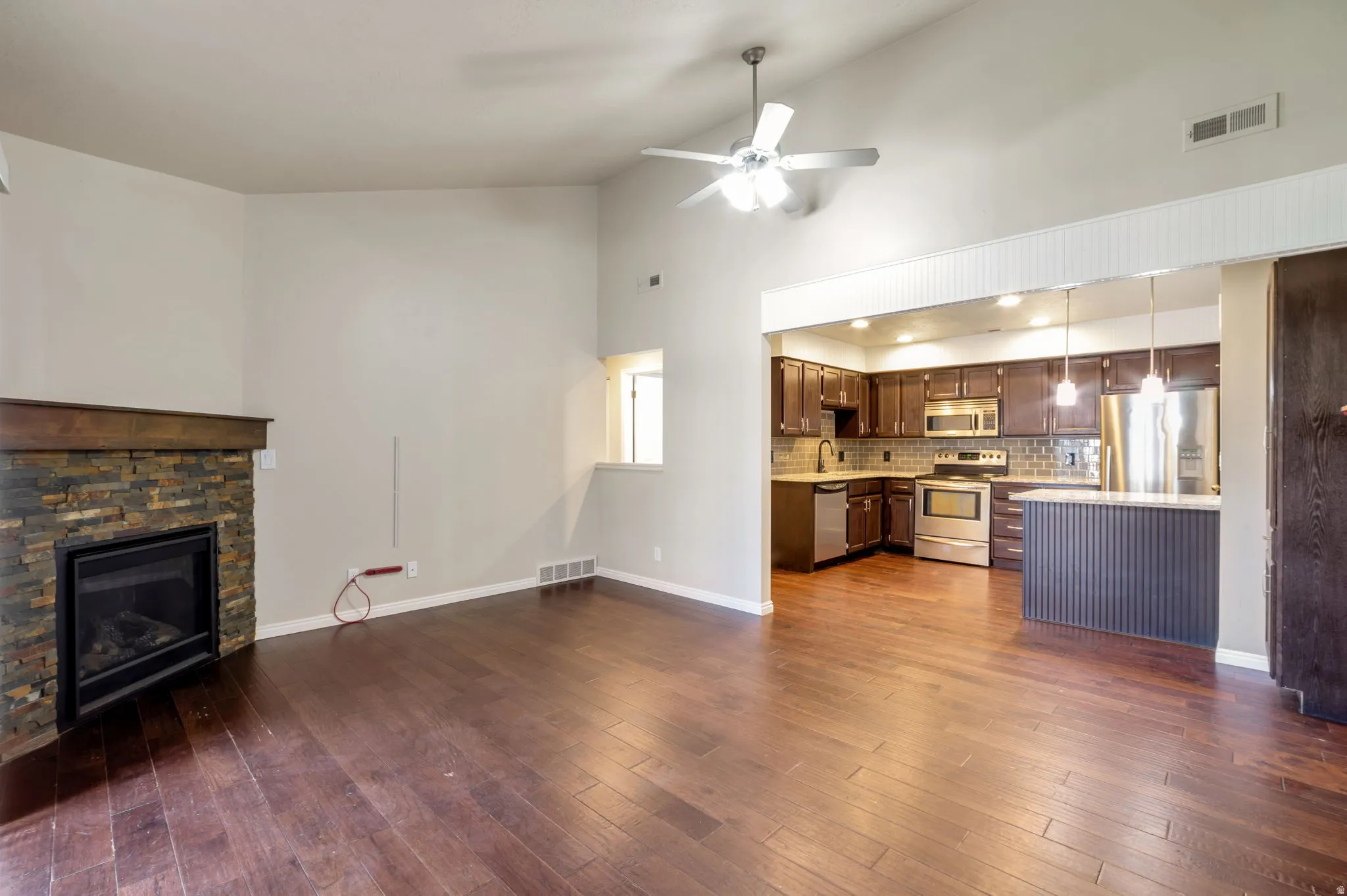 Spacious living area featuring high vaulted ceilings, wood-finish flooring, and a stone-clad fireplace with a wood mantel