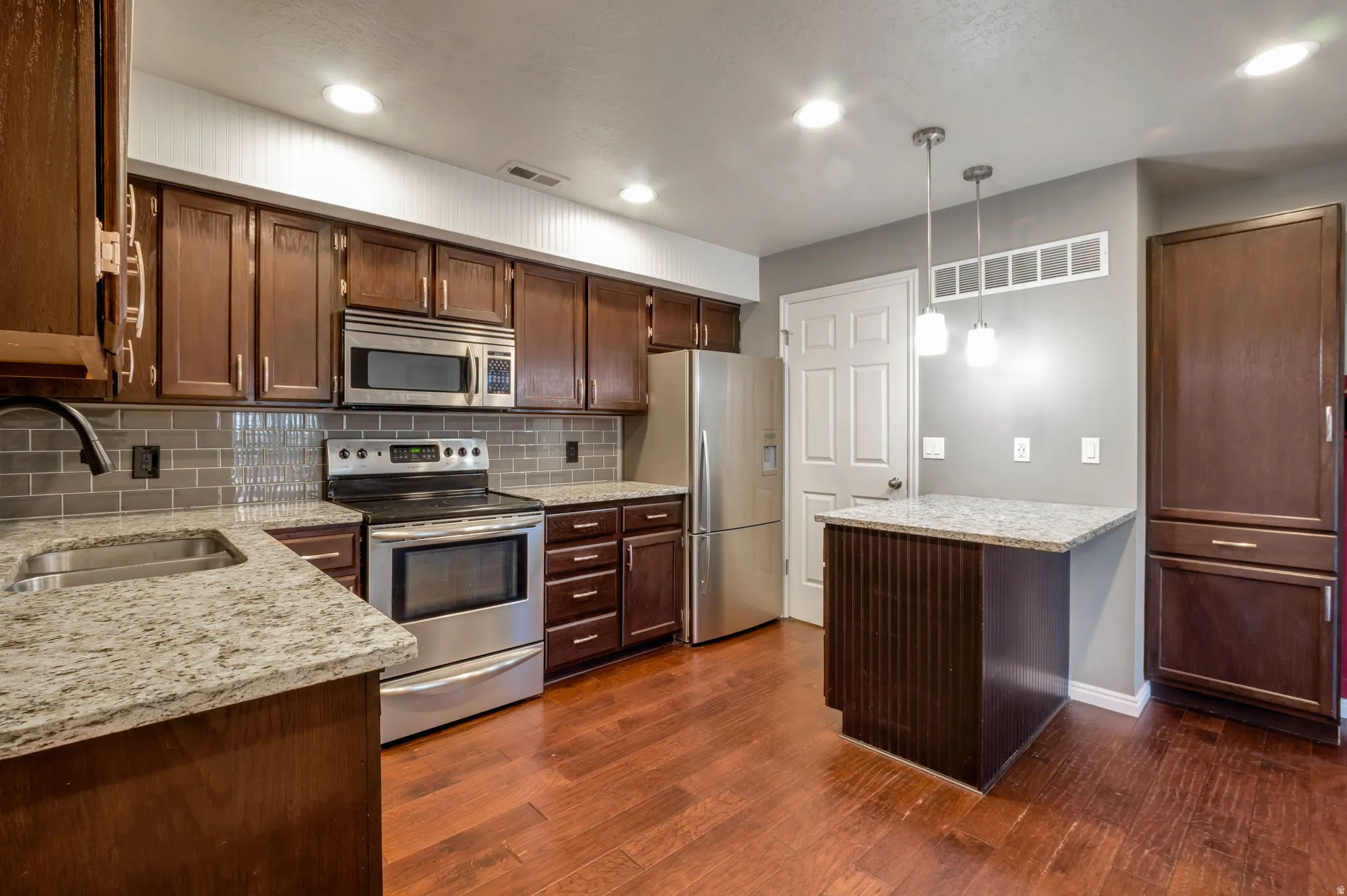 Kitchen featuring wood-finish flooring, granite countertops, stainless steel appliances, a tiled backsplash, and recessed lighting