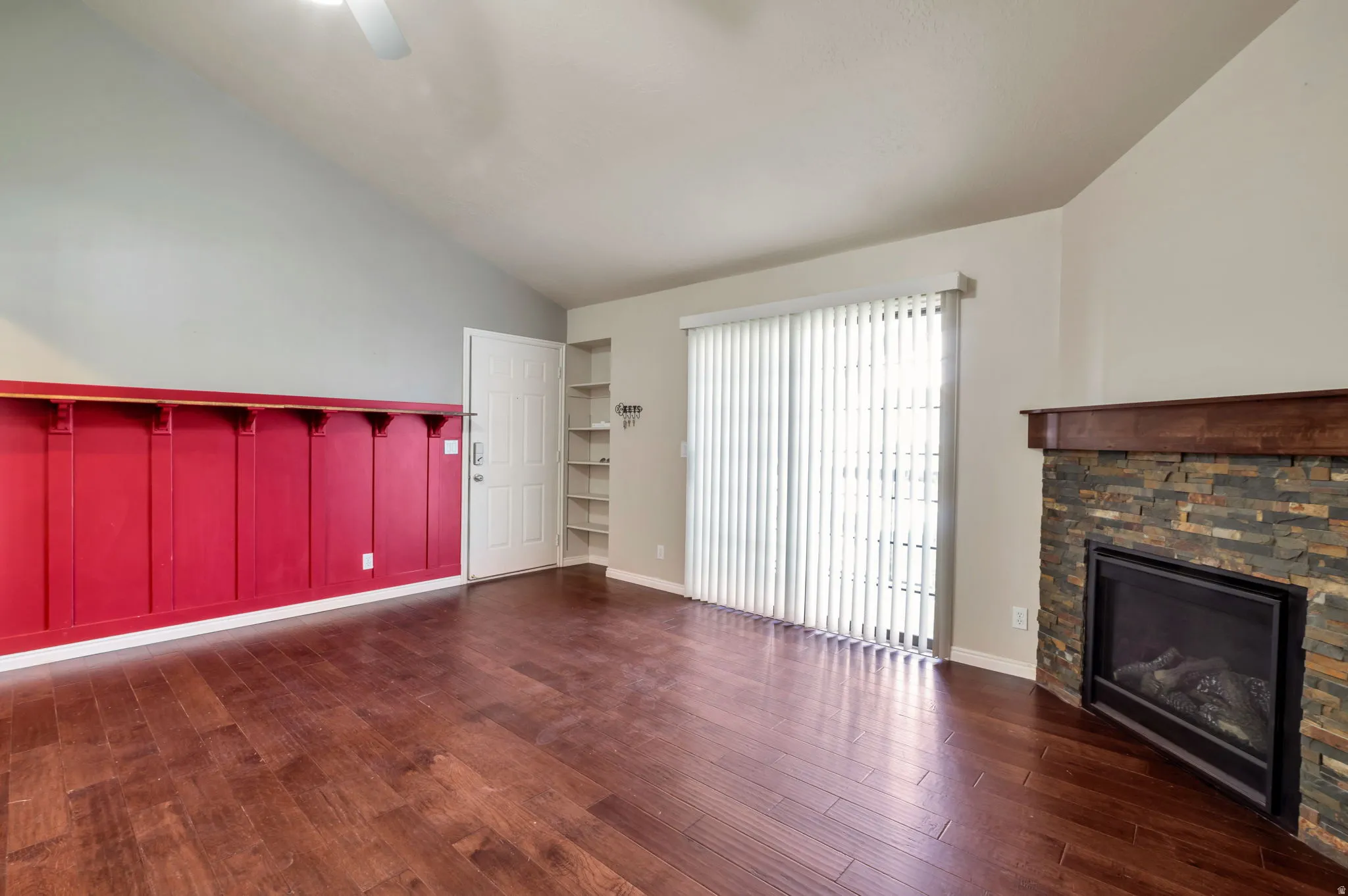 Spacious living area featuring rich wood-finish flooring, a vaulted ceiling, and a corner fireplace with a stacked stone surround and wood mantel