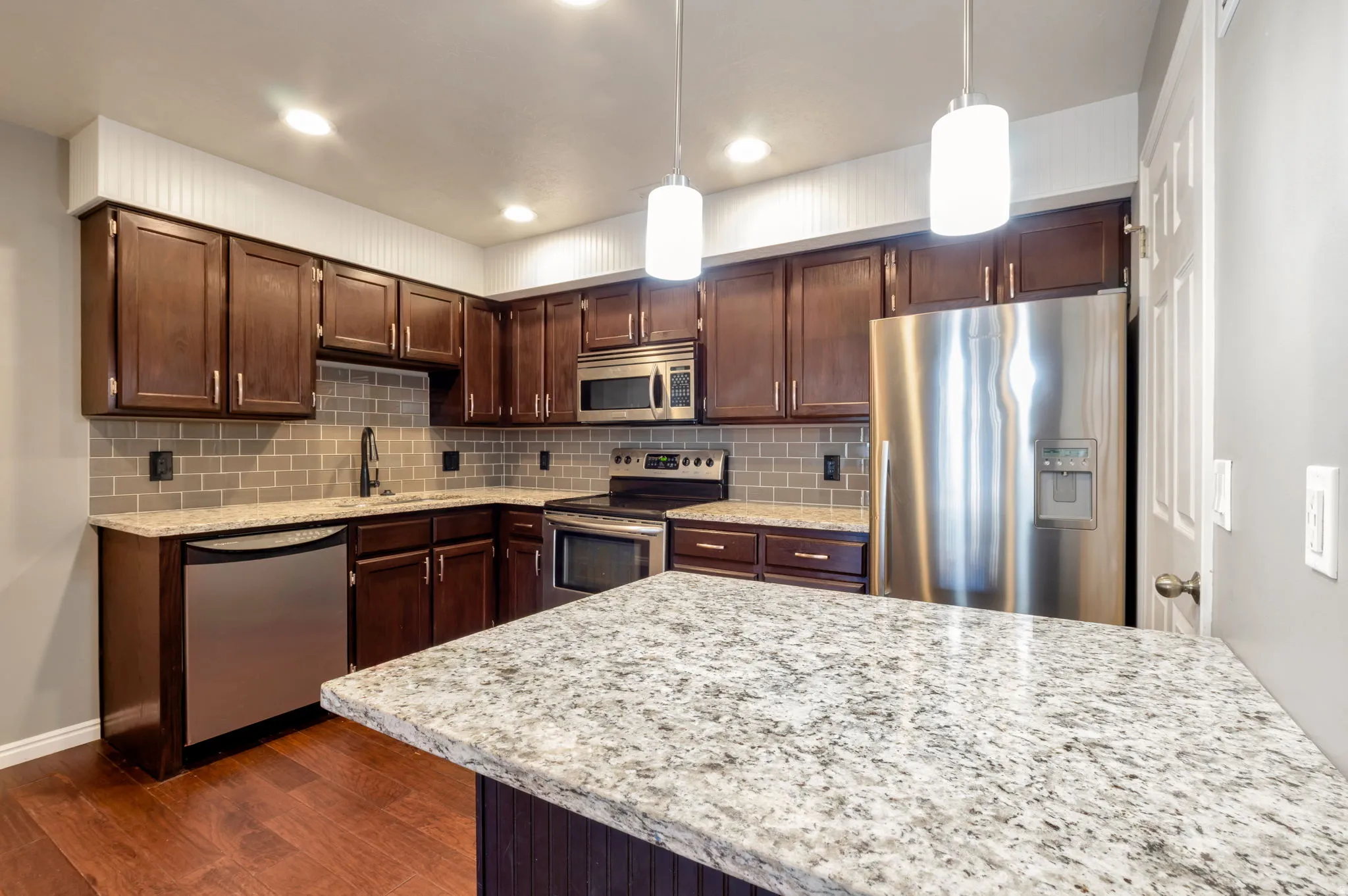 Kitchen featuring dark wood cabinetry, stainless steel appliances, a subway tile backsplash, and light-toned countertops