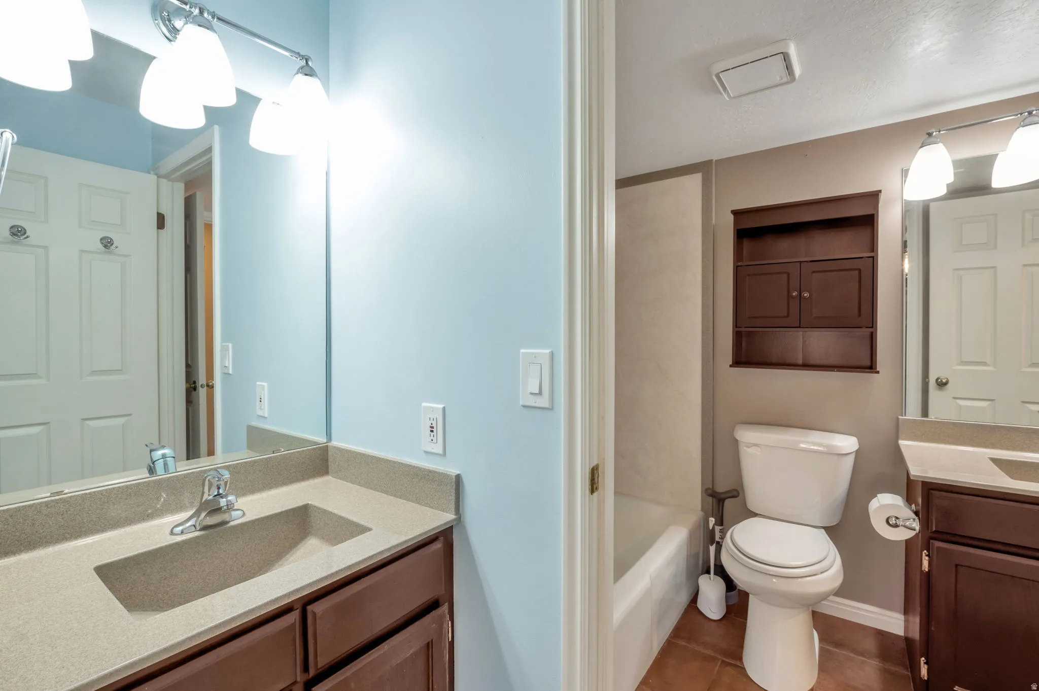 Bathroom featuring a vanity with an integrated sink, a large mirror with a three-light fixture, a built-in wooden cabinet, and a bathtub with a shower