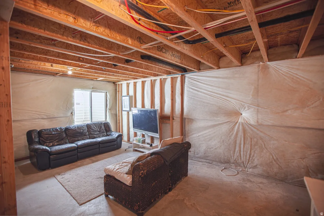 Unfinished basement space featuring exposed wood joists and subflooring, framed walls with insulation, and a concrete floor