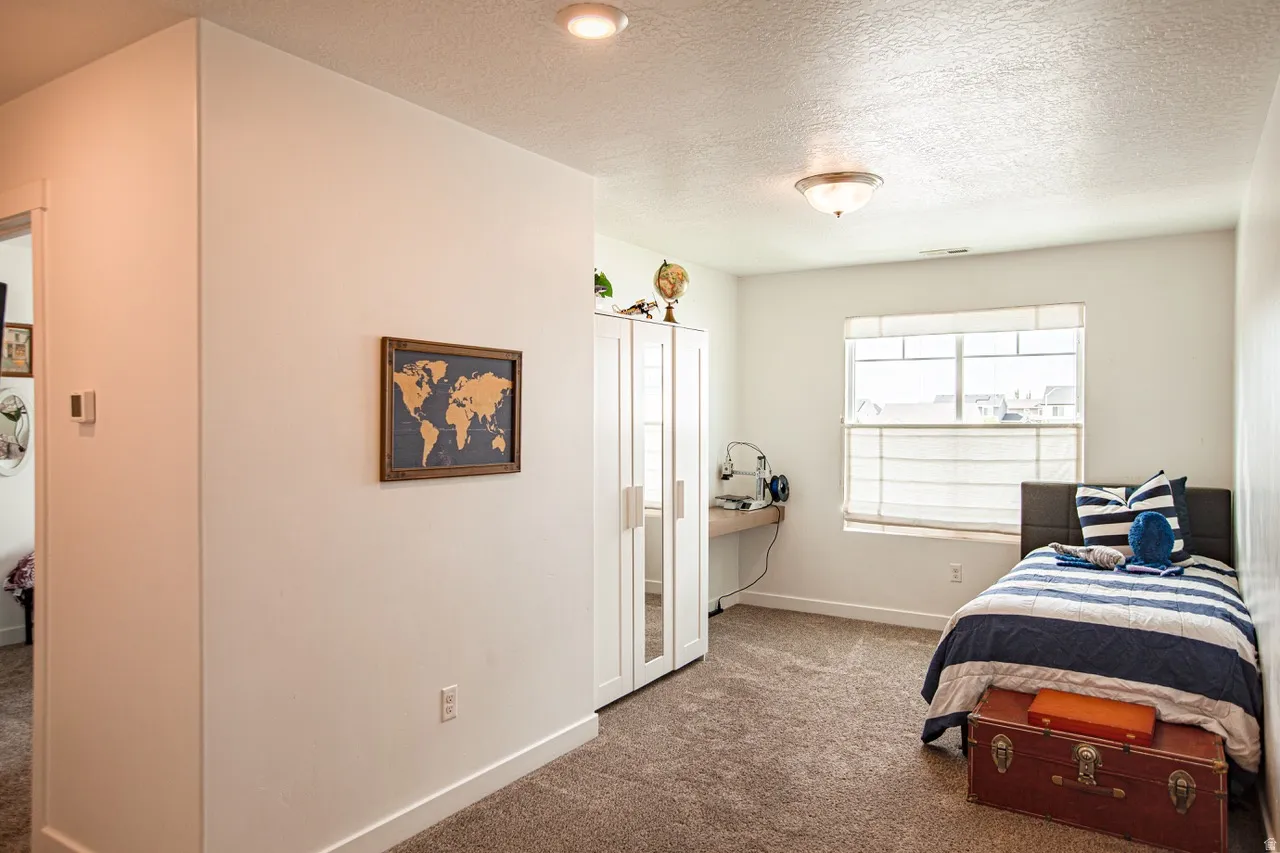 Carpeted room featuring a single window with blinds, a built-in desk, and a built-in wardrobe with mirrored doors
