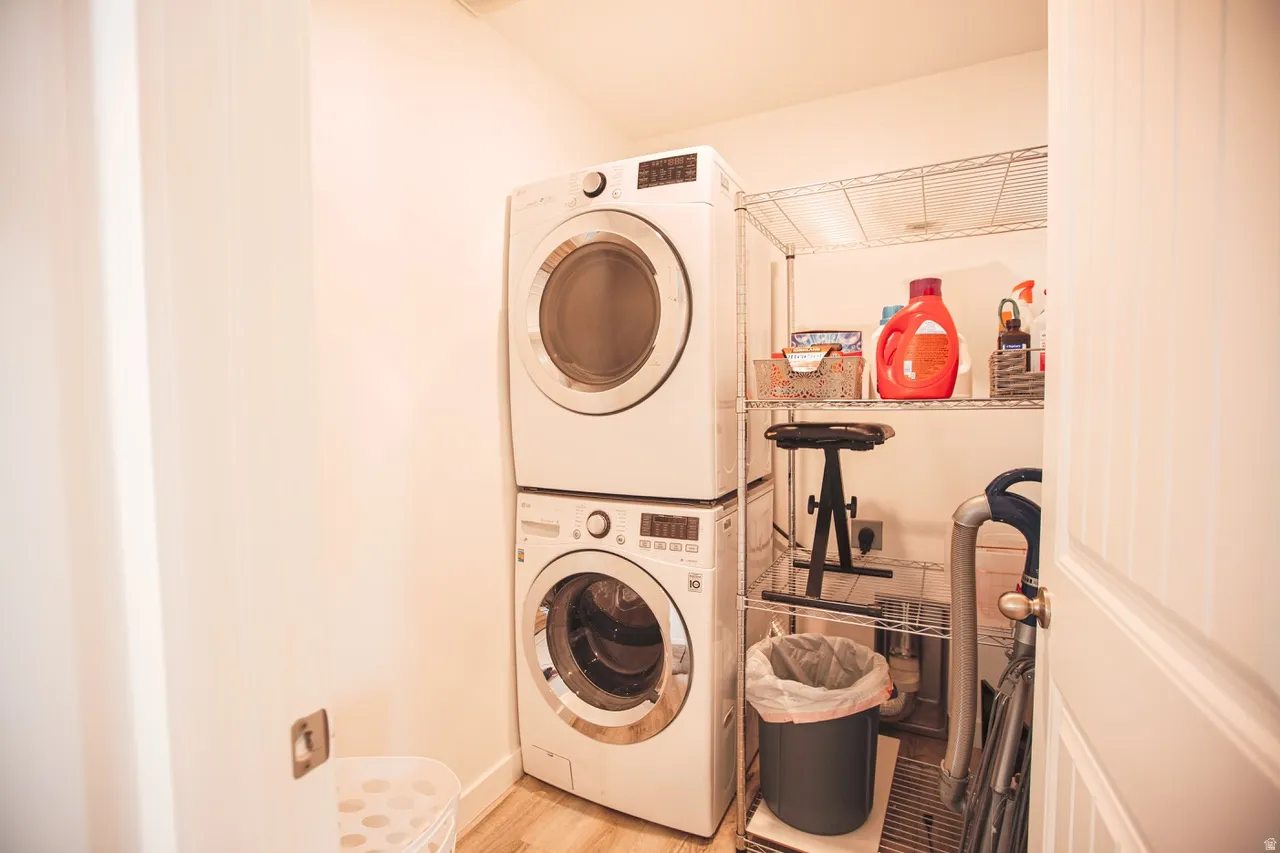 Dedicated laundry closet featuring a stackable washer and dryer, wood-finish flooring, and built-in wire shelving