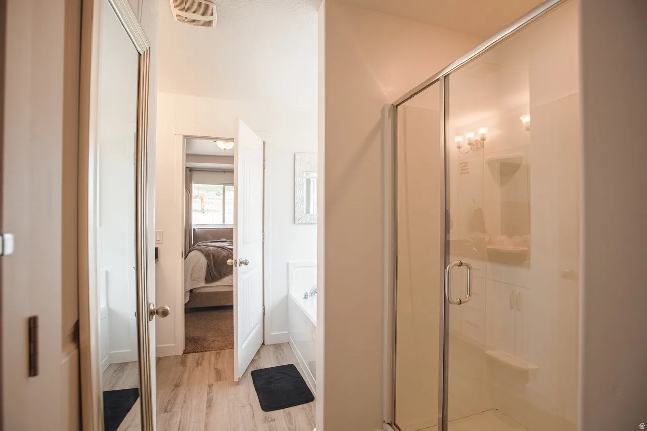 Bathroom featuring a glass-enclosed shower, built-in bathtub, and wood-finish flooring
