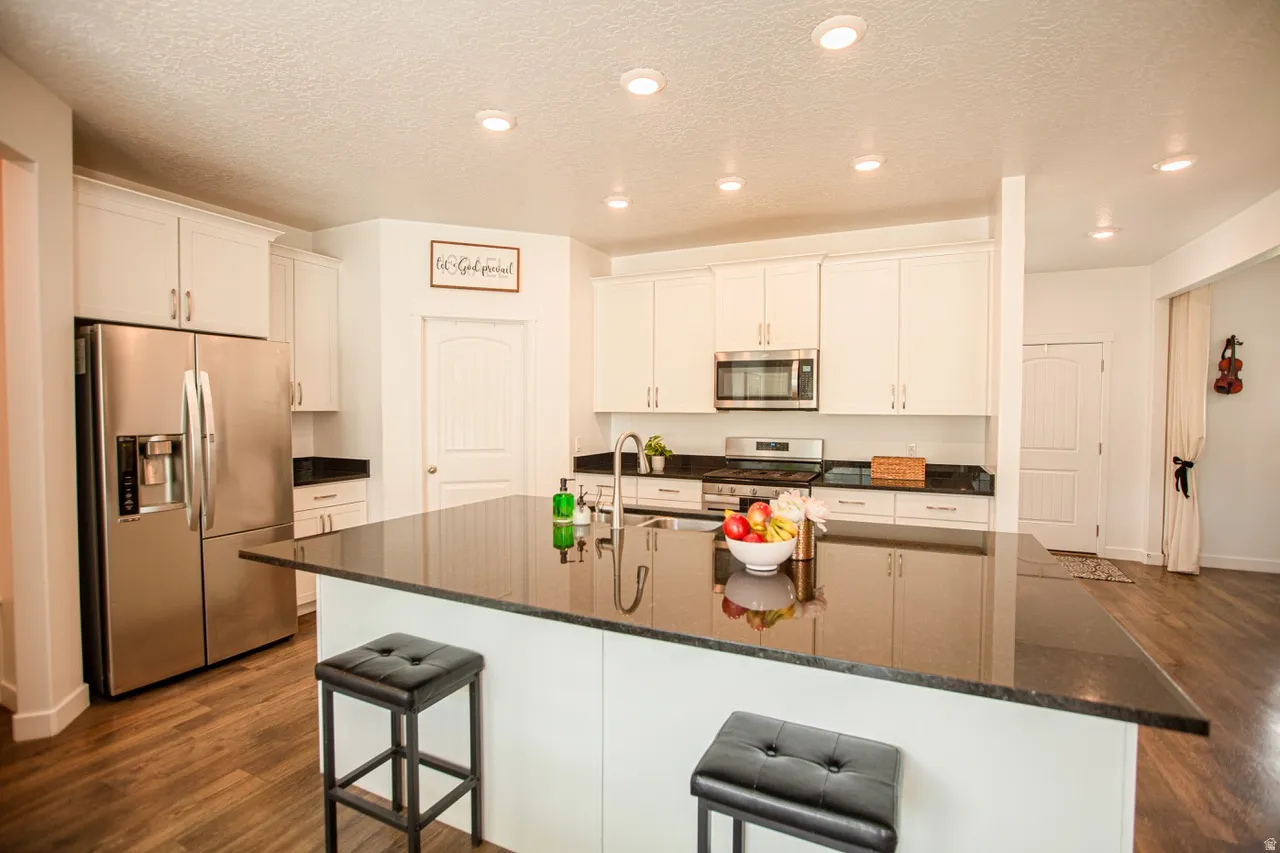 Contemporary kitchen featuring a large central island with a dark countertop, white cabinetry, stainless steel appliances, recessed lighting, and wood-finish flooring