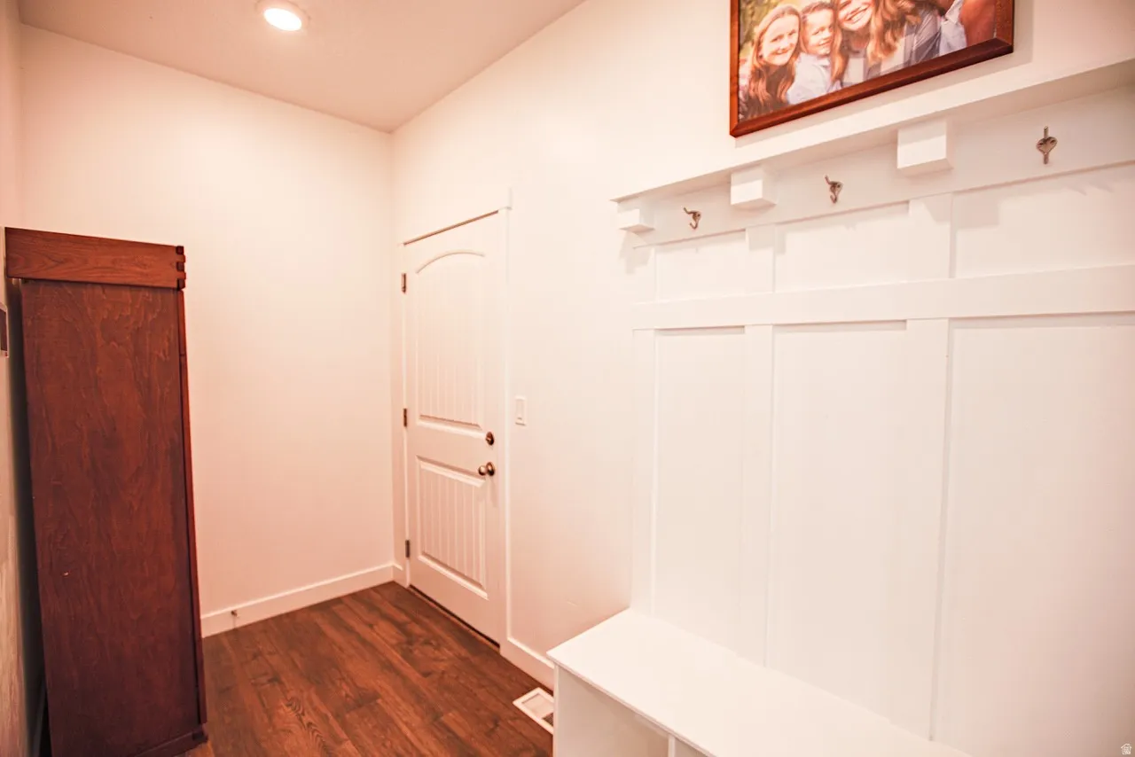 Entryway featuring wood-finish flooring, a white paneled door with an arched top, and a built-in white board-and-batten wall with integrated hooks and bench seating