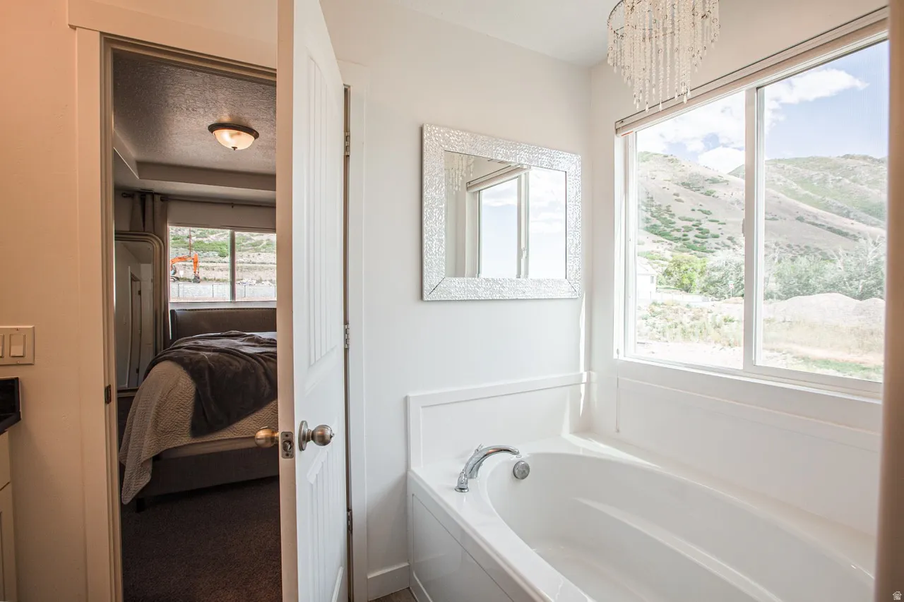 Soaking tub with a polished chrome faucet, a decorative framed mirror, and a crystal chandelier