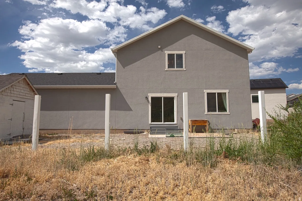 Rear facade of a stucco home featuring a sliding glass door, multiple windows, and a black shingle roof