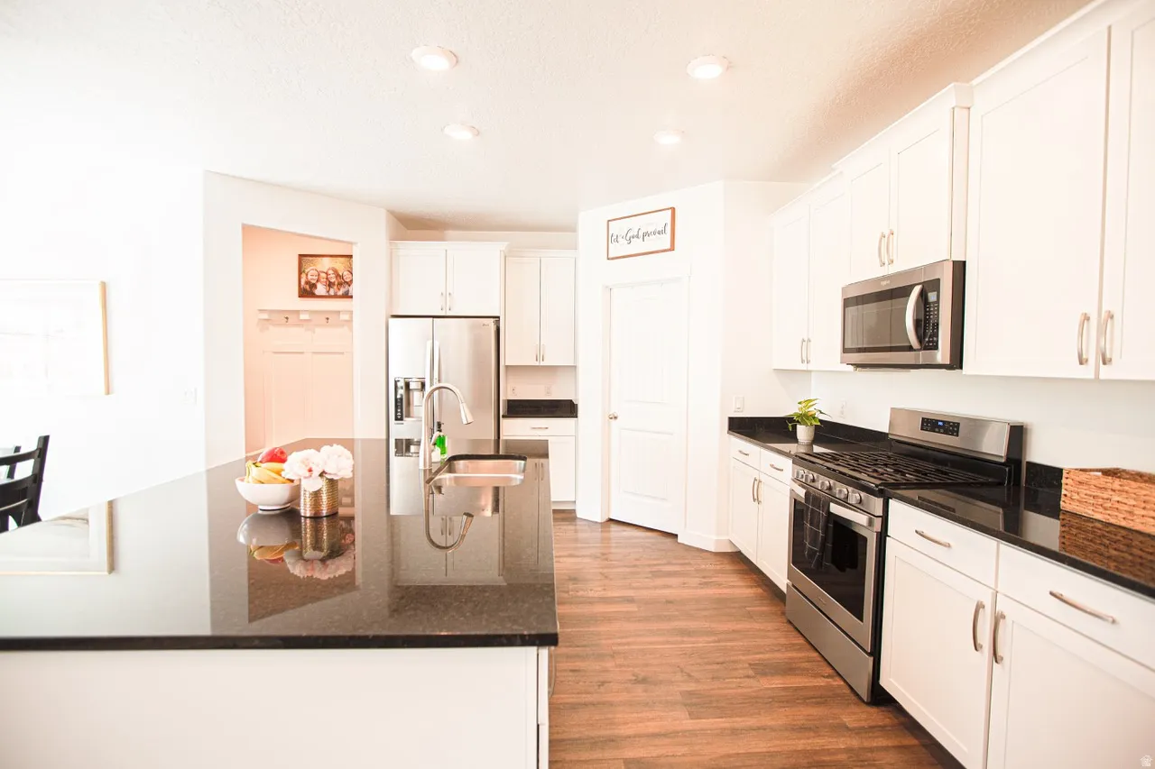 Kitchen featuring an expansive island with an undermount sink, dark countertops, white cabinetry, stainless steel appliances, and wood-finish flooring