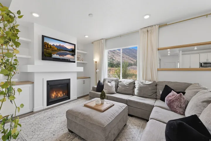 Integrated fireplace with mantel, built-in shelving, recessed lighting, expansive window, and wood-finish flooring