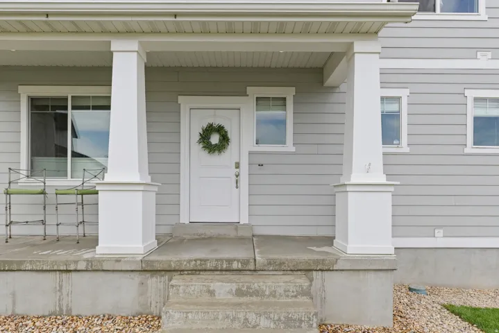 Entry featuring a covered porch with white columns, concrete steps, and light gray horizontal siding