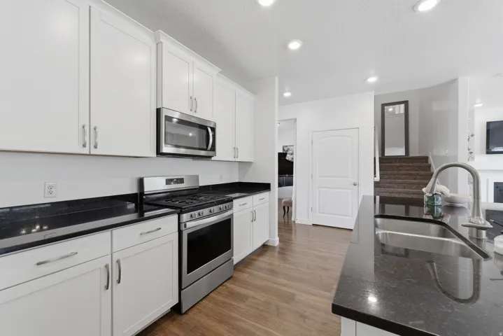 White cabinetry, dark countertops, stainless steel appliances, wood-finish flooring, and recessed lighting