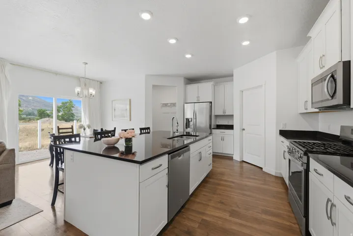 Modern kitchen featuring white cabinetry, stainless steel appliances including a gas range and refrigerator, black countertops with a waterfall-edge island, recessed ceiling lighting, wood-finish flooring, and abundant natural light from sliding glass doo