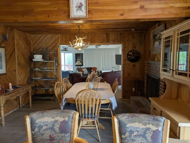 Dining area featuring wood-paneled walls, wood-finish flooring, and a fireplace with a brick surround