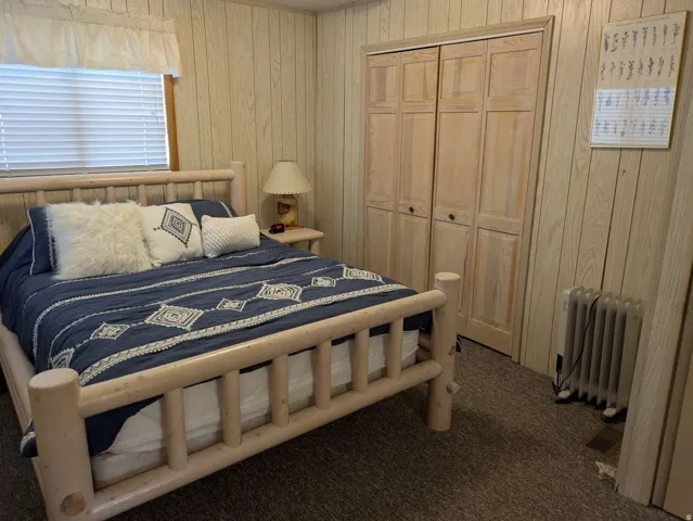 Wood-paneled interior walls, window with blinds, bi-fold closet doors, and carpet flooring