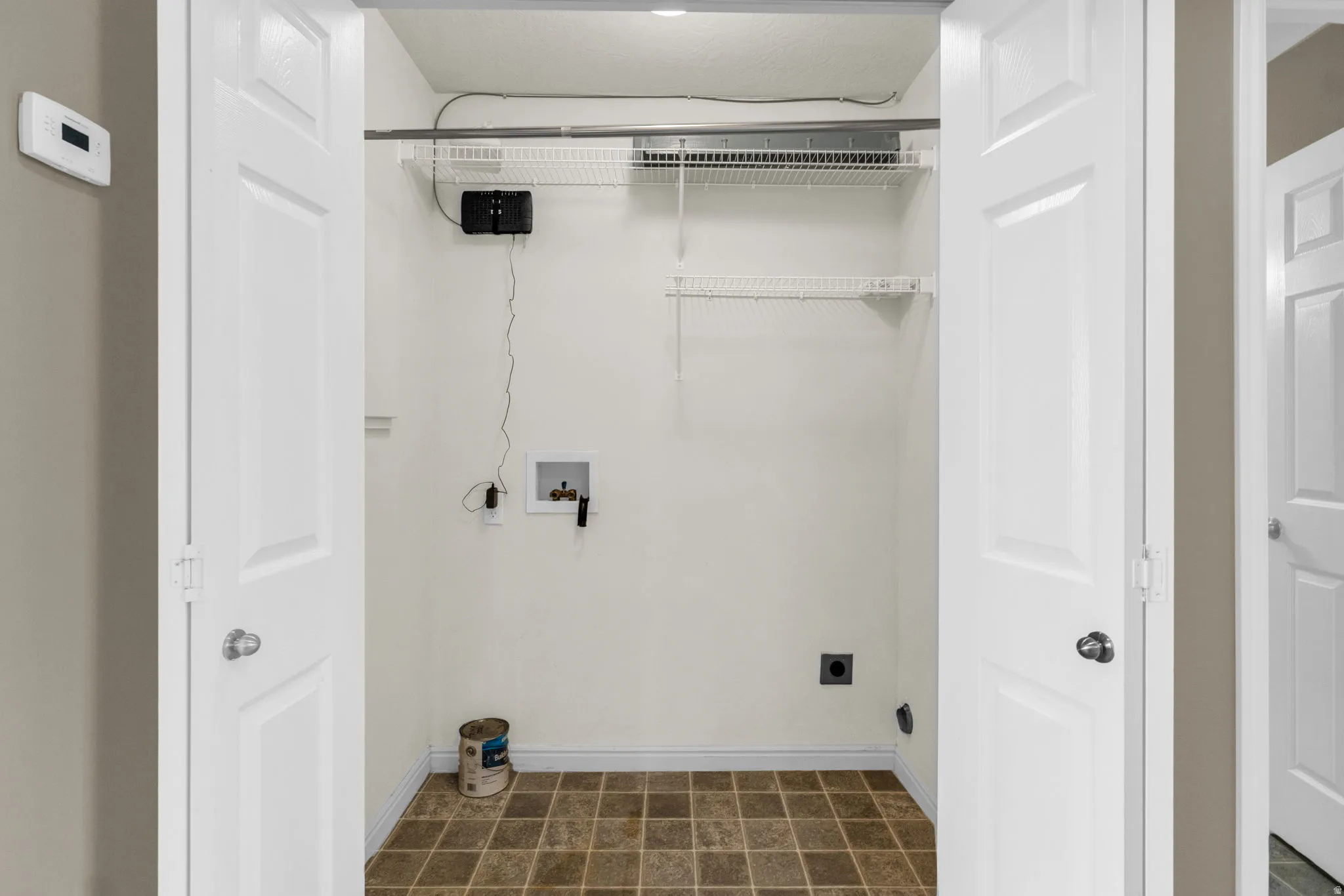 Utility closet with vinyl tile flooring, white walls, and built-in wire shelving.