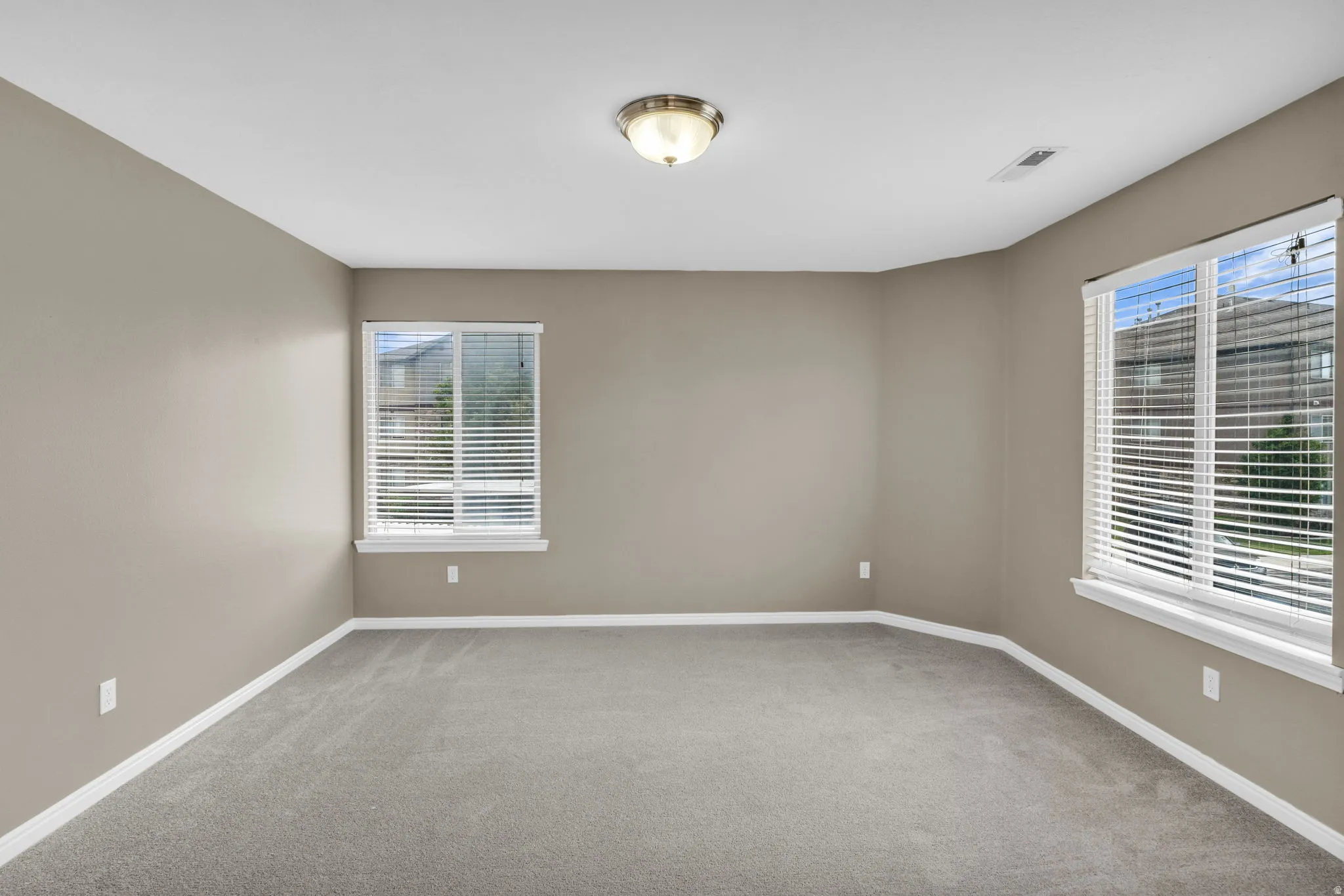 Spacious room featuring neutral painted walls, light grey carpeting, and white baseboards.
