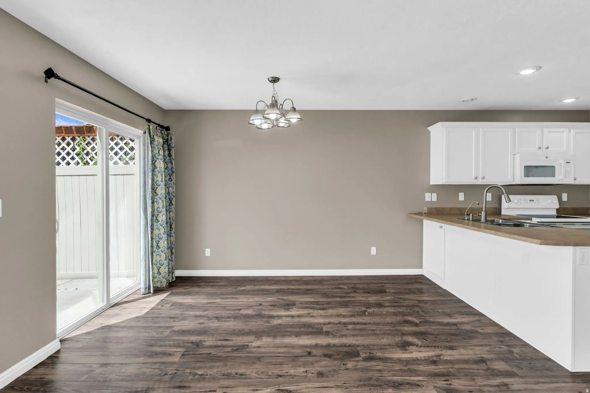 Open-concept kitchen and dining area featuring wood-finish flooring, white cabinetry, a kitchen island with sink, and a sliding glass door.