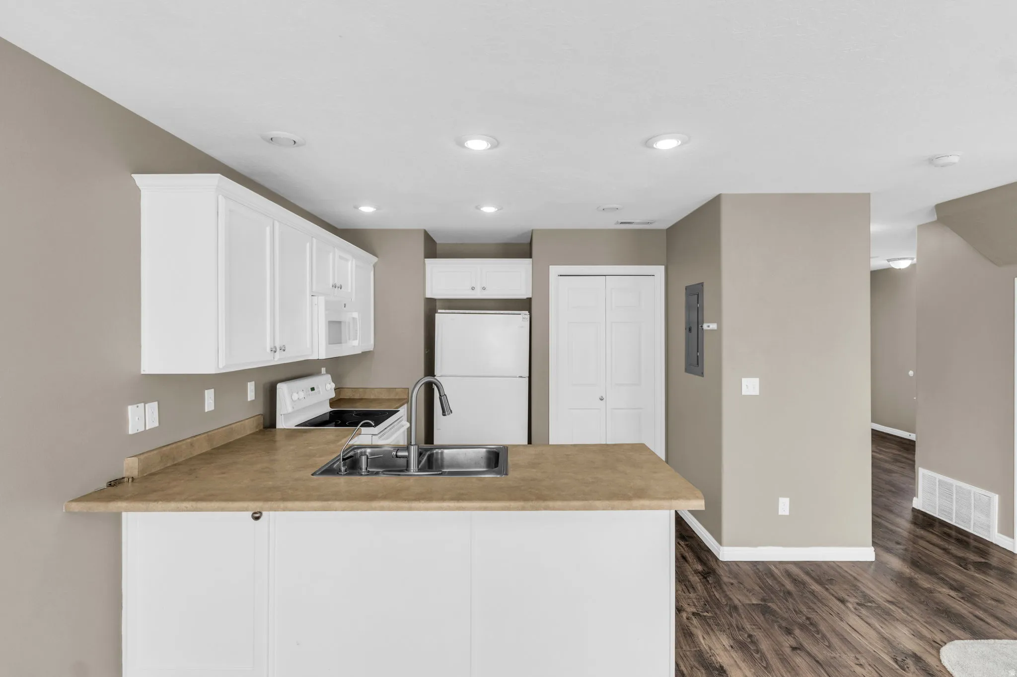 Open-concept kitchen featuring white cabinetry, light-toned countertops, and a double-basin stainless steel sink with a high-arc faucet.