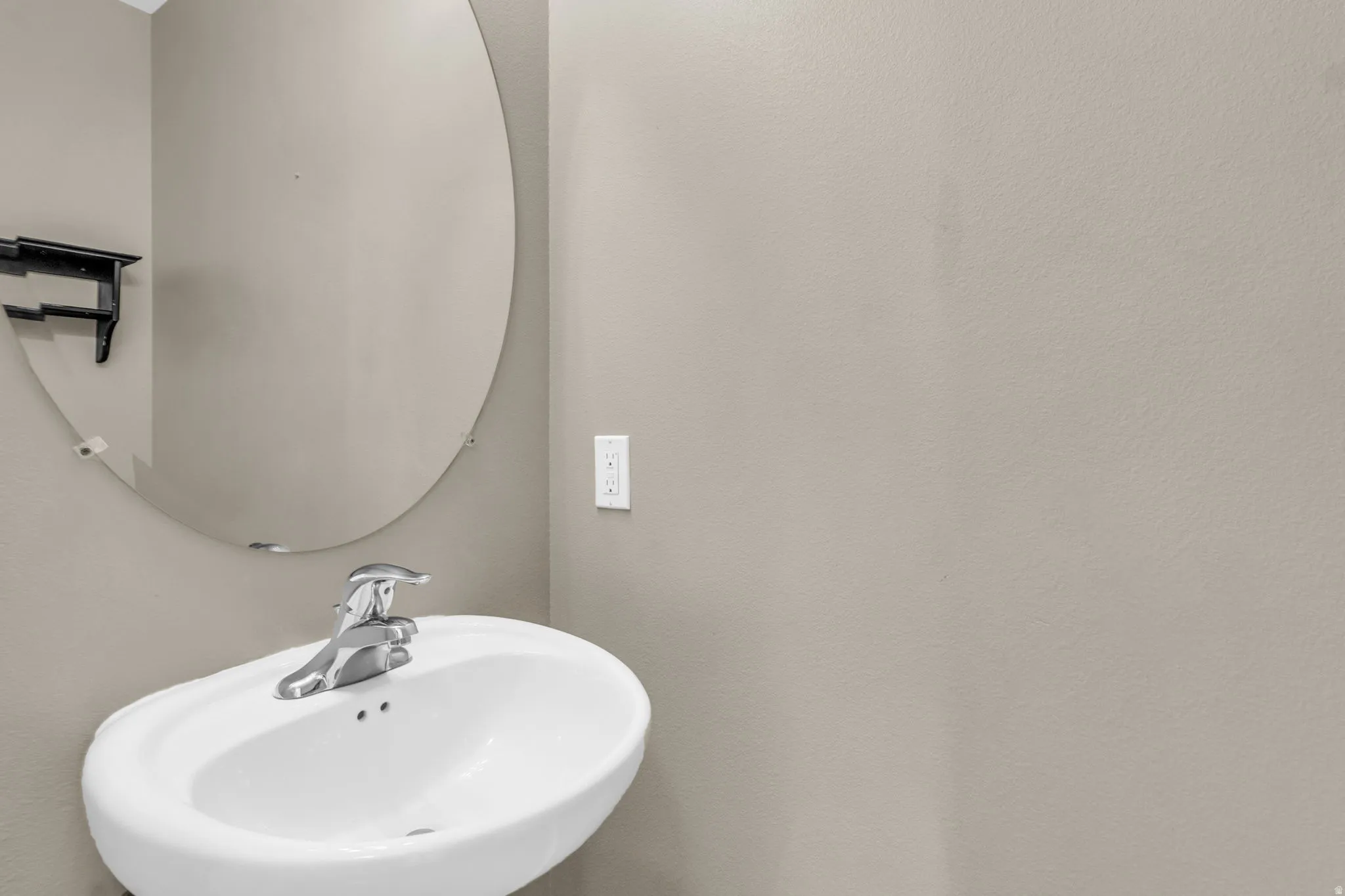 Pedestal sink with chrome-finish faucet and an oval wall mirror.