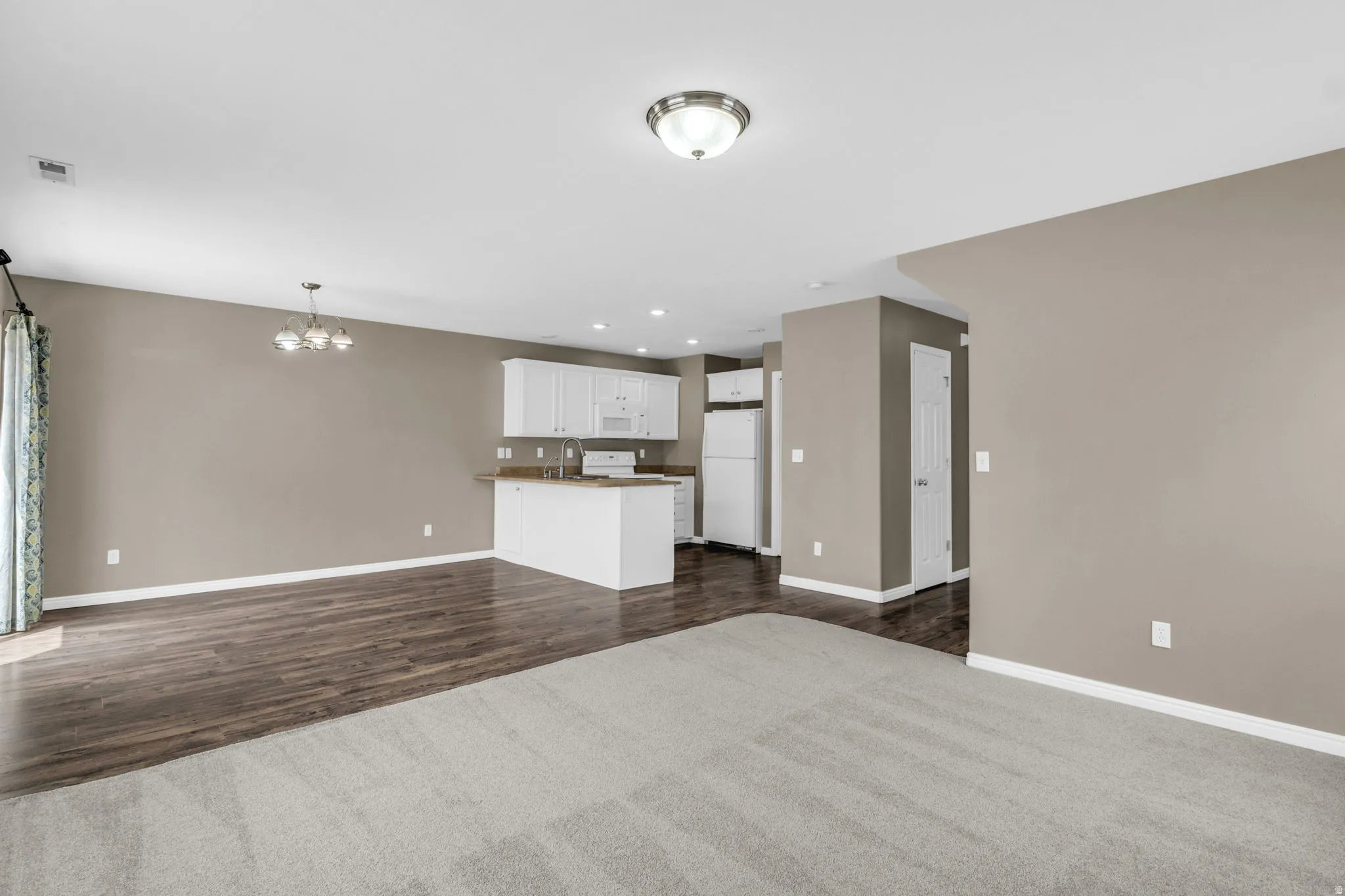 Open-concept living space featuring light gray walls and a combination of gray carpet and wood-finish flooring.