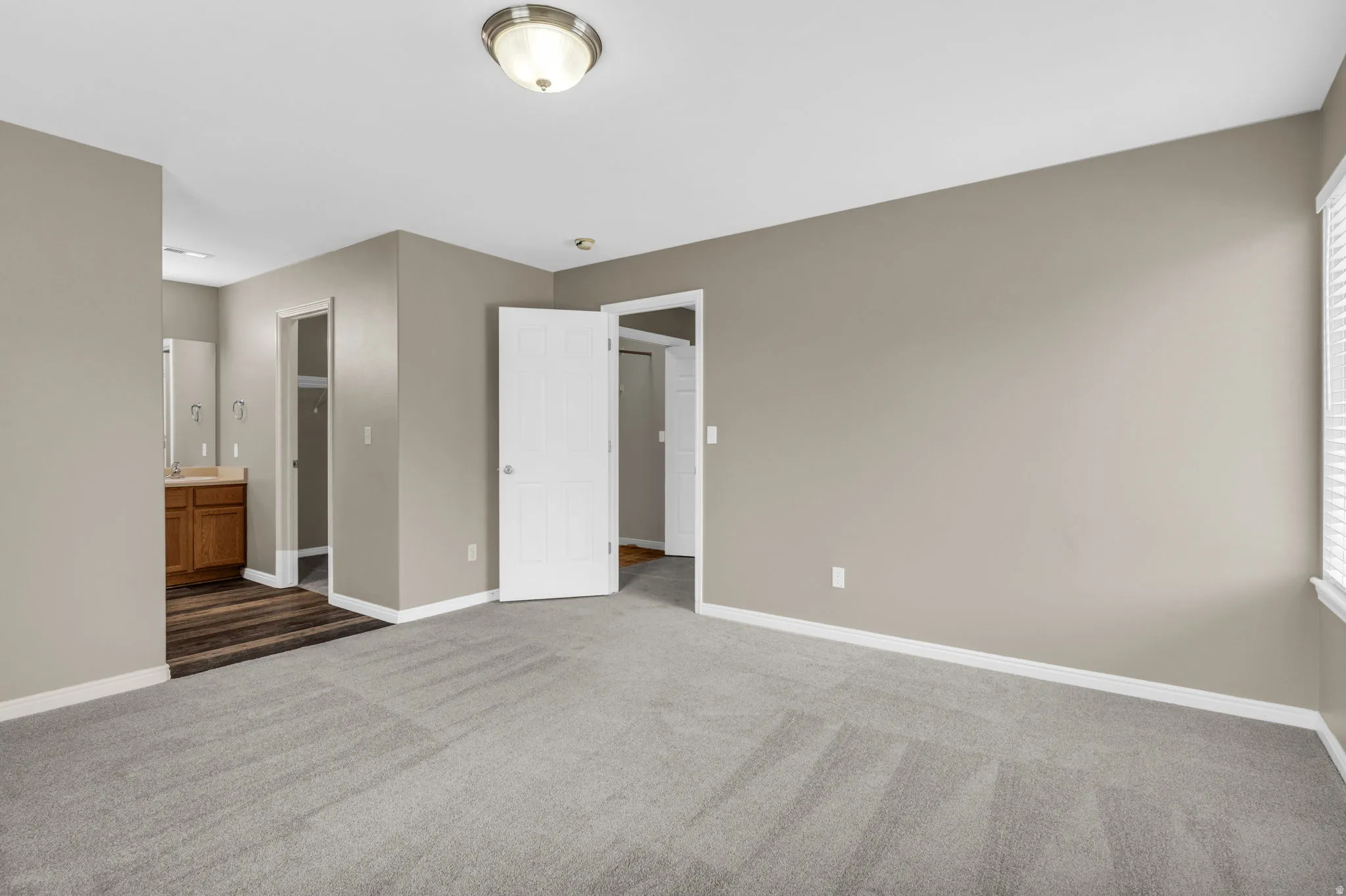 Spacious ensuite primary bedroom featuring neutral carpeting, soft light-toned walls, and crisp white trim for a bright and inviting feel.