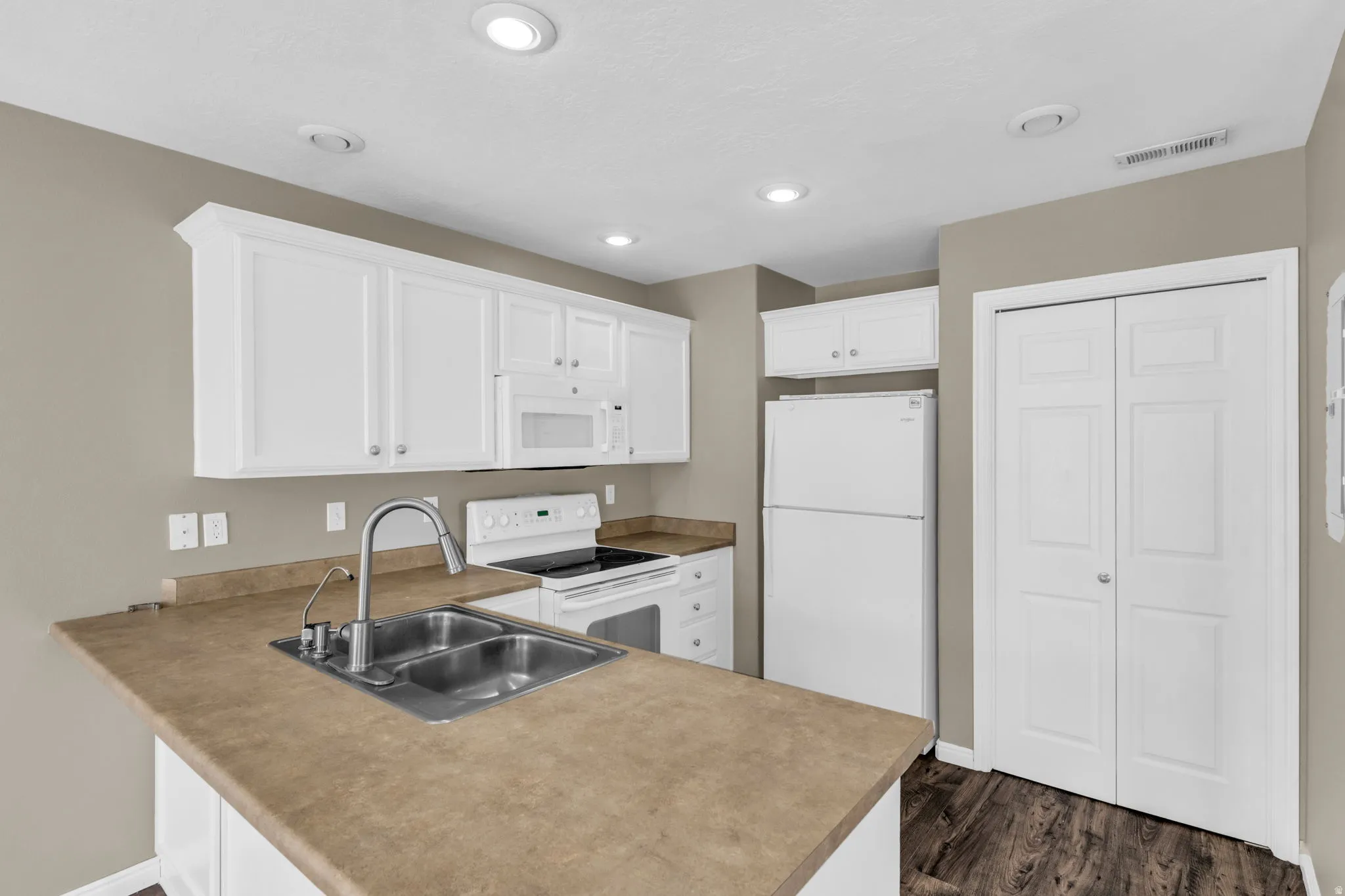 Modern kitchen featuring white cabinetry, a double basin stainless steel sink, built-in microwave, and a full-size refrigerator.