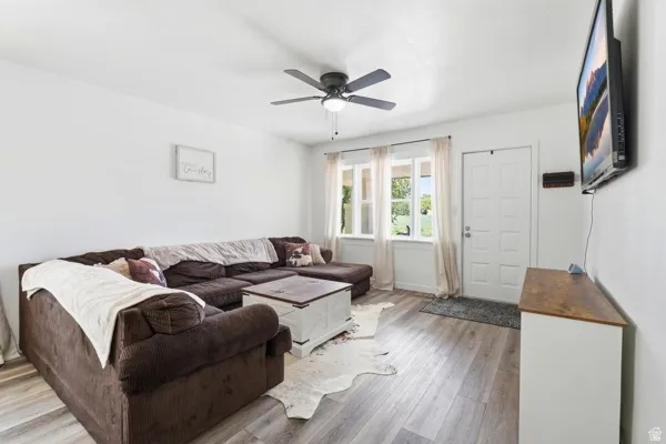 Living area featuring wood-finish flooring, white walls, and a ceiling fan with integrated lighting