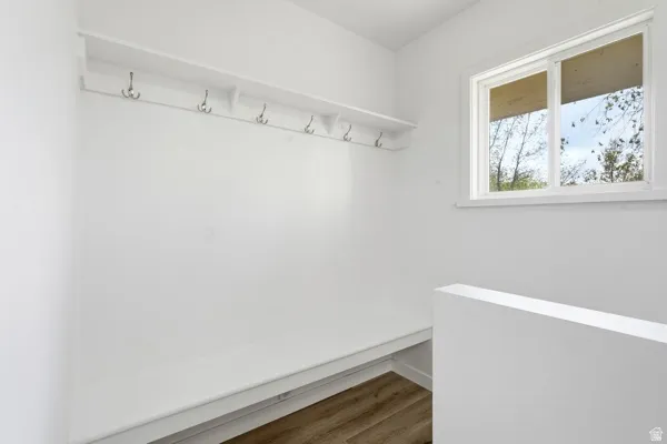 Entryway featuring a built-in bench, wall-mounted shelf with hooks, wood-finish flooring, and a window providing natural light