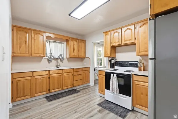 Kitchen featuring wood cabinetry, light-toned countertops, a stainless steel sink with a high-arc faucet, and wood-finish flooring