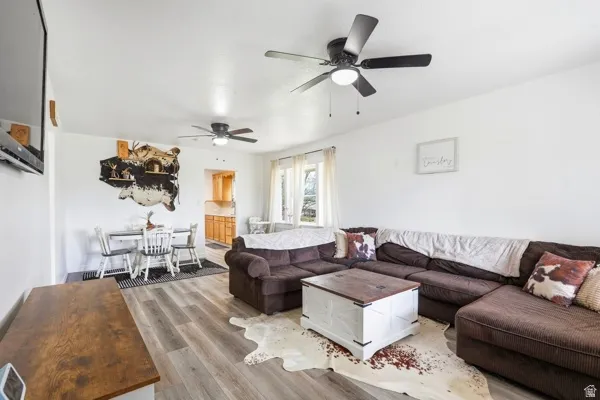 Open-concept living space featuring wood-finish flooring, white walls, and two ceiling fans with integrated lighting