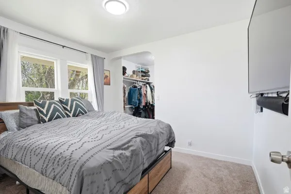 Carpeted room featuring a double-paned window, built-in closet with shelving and hanging rods, ceiling-mounted light fixture, and white baseboards