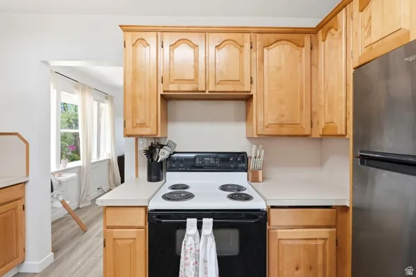 Kitchen featuring light wood cabinetry, white countertops, black electric range, and a stainless steel refrigerator