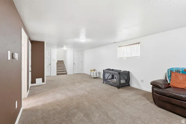 Spacious lower-level room featuring light-colored carpeting, white walls, and a window with white blinds