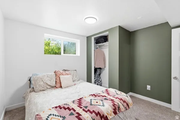 Carpeted room featuring a double-paned window, neutral wall paint, accent wall, and an integrated closet with shelving and hanging rod