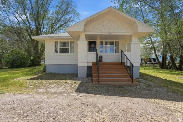 White exterior with a covered porch featuring wood steps and black metal railings