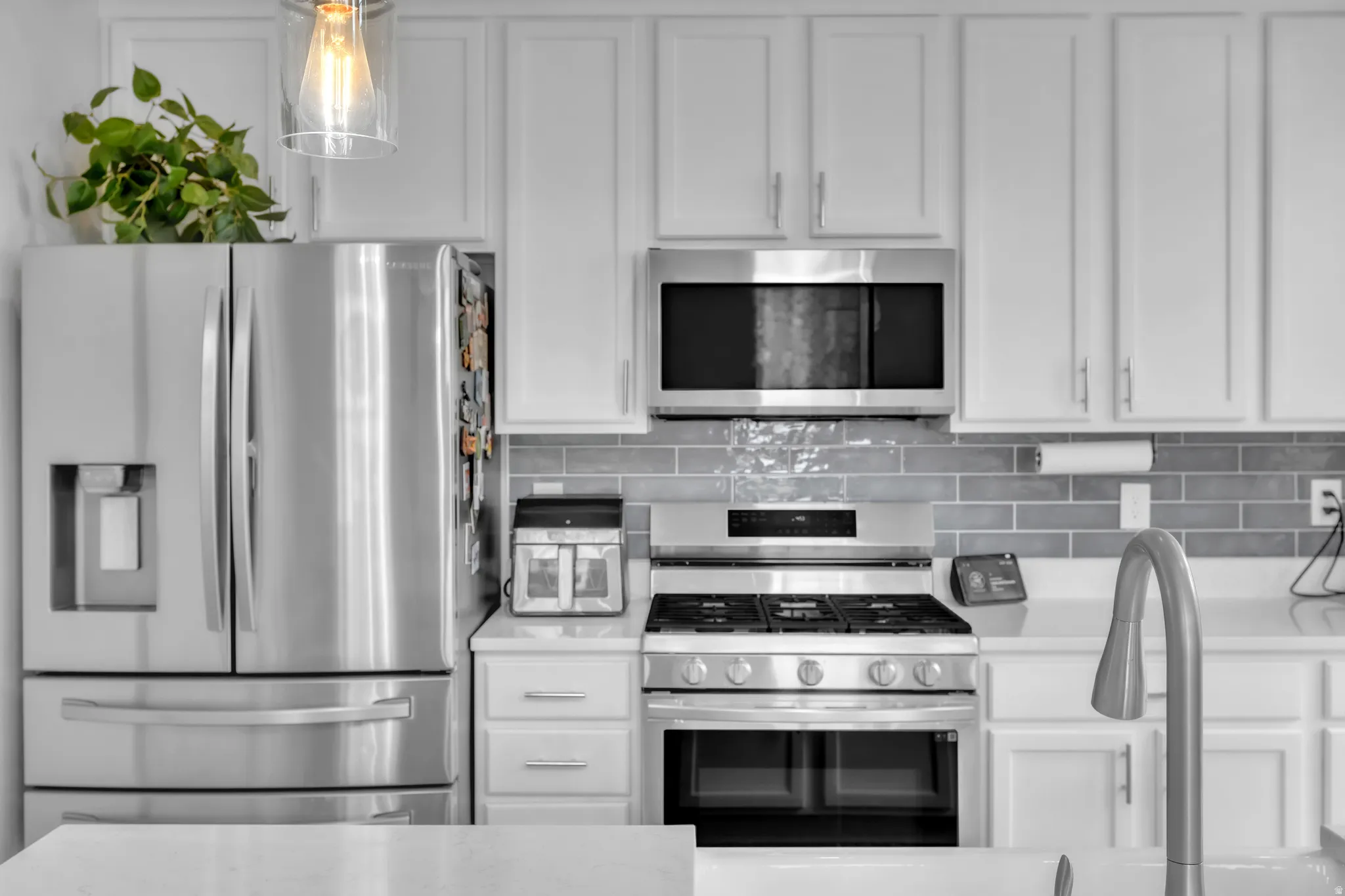 Modern kitchen featuring white cabinetry, stainless steel appliances, grey subway tile backsplash, and light-toned countertops