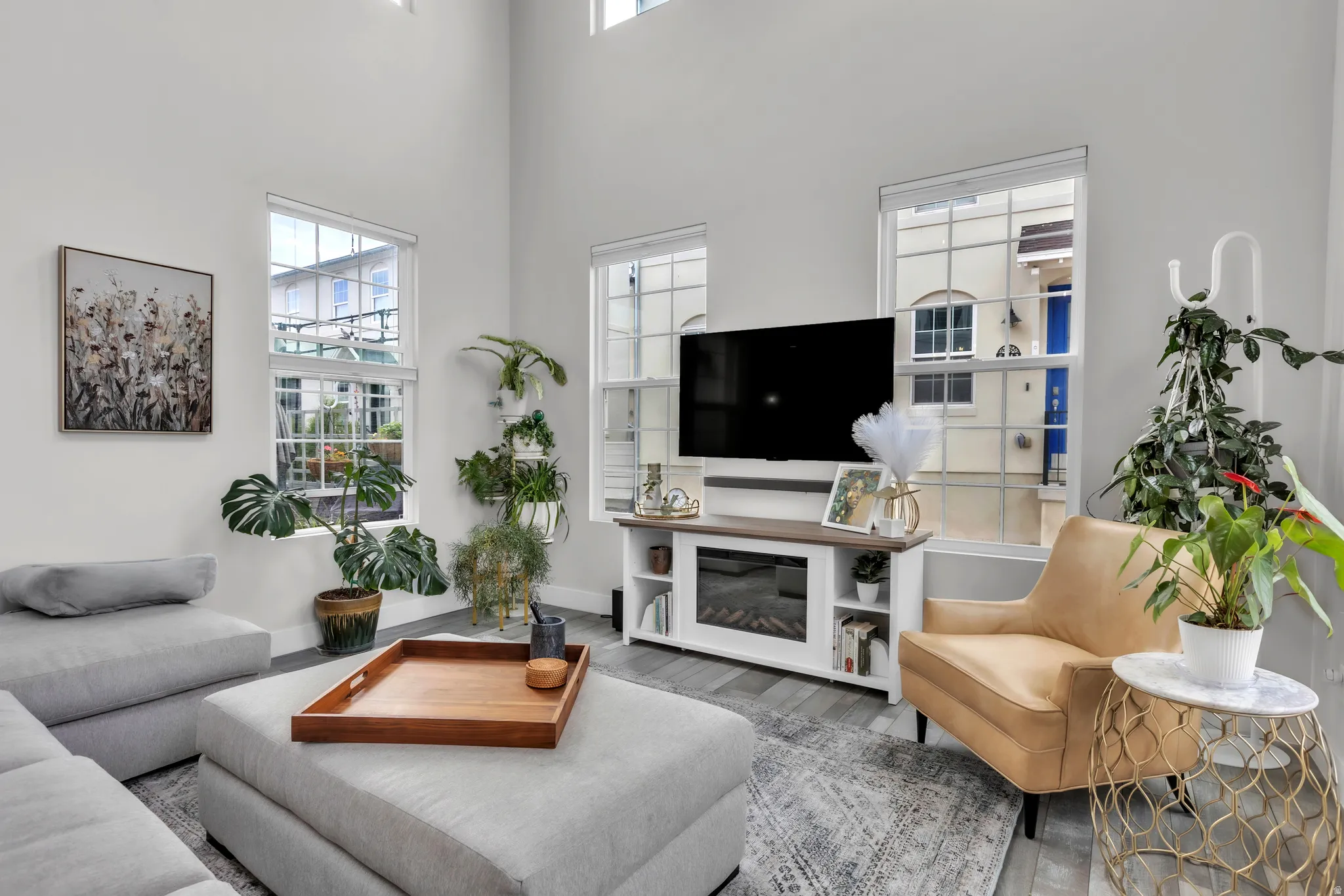 Living area featuring a soaring ceiling, wood-finish flooring, multiple large windows, and a built-in media console with an electric fireplace