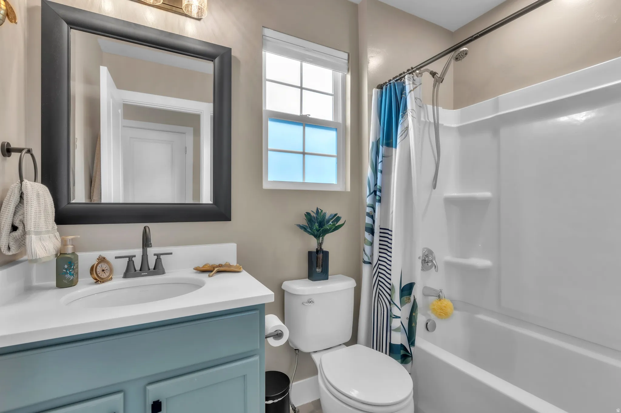 Bathroom featuring a light blue vanity with a white countertop and oval undermount sink, matte black faucet, and a framed wall mirror