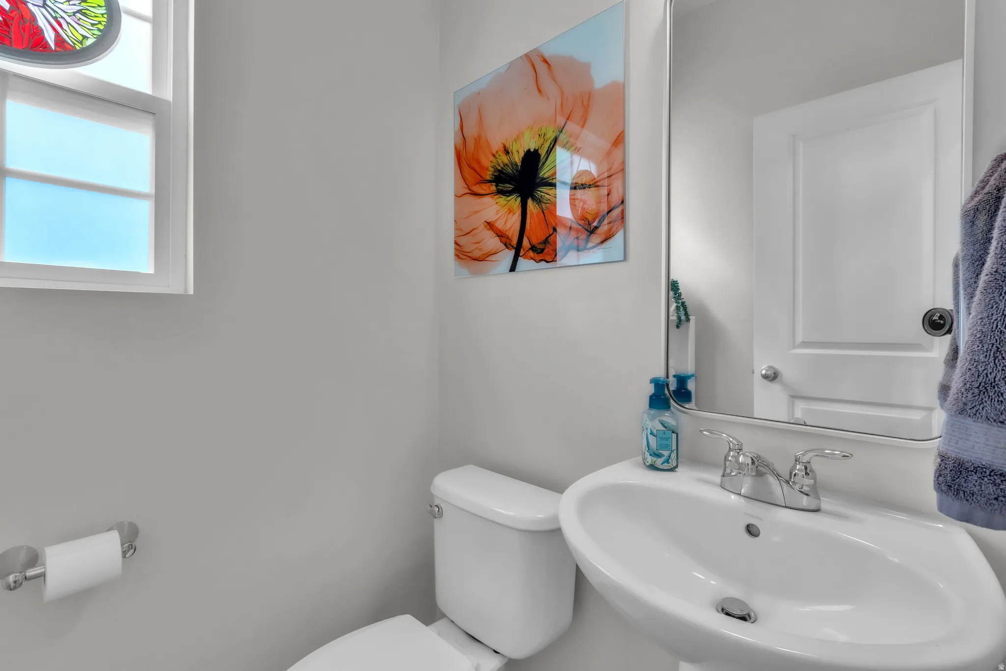 White pedestal sink with chrome faucet, white toilet, and a window with frosted lower panes
